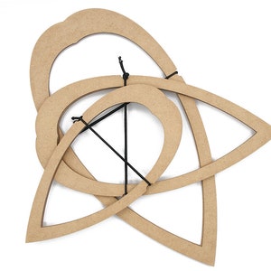 Puede incluir: Arte mural de madera con un diseño abstracto de formas entrelazadas. La obra de arte incluye una forma grande y redondeada, una forma de lágrima y una forma circular, todas conectadas con una cuerda negra. La madera tiene un color marrón claro natural.