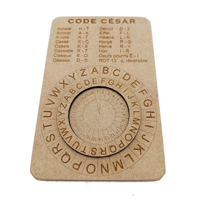 Puede incluir: Una rueda de cifrado César de madera con el texto "CODE CÉSAR" en la parte superior. La rueda de cifrado tiene dos discos circulares giratorios con letras y números. El disco exterior tiene el alfabeto, y el disco interior tiene un alfabeto más pequeño.