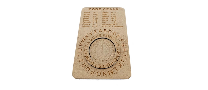 May include: A wooden Caesar cipher wheel with the text "CODE C&Eacute;SAR" at the top. The cipher wheel has two rotating circular discs with letters and numbers. The outer disc has the alphabet, and the inner disc has a smaller alphabet. The cipher is on a rectangular wooden base.