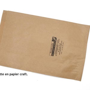 May include: A brown craft paper envelope with a small black logo and text. The rectangular envelope is sealed. The text at the bottom of the image reads: "Le jeu est emball&eacute; dans une pochette en papier craft."