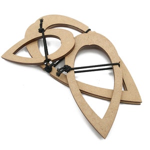 Può includere: Tre cornici in legno a forma di goccia, collegate da cordini neri. Le cornici sono marrone chiaro e disposte in una configurazione a strati su uno sfondo bianco. Il design suggerisce un elemento decorativo o artigianale.