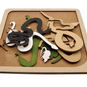 May include: A wooden puzzle with snake-like shapes in black, white, green, and tan. The pieces are within a square frame, creating a layered effect. The design is intricate and artistic, suitable for educational or decorative purposes. The puzzle is made of wood.