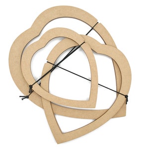 May include: Three interlocking heart-shaped wooden craft forms in varying sizes. The forms are a light brown color and are held together with black string. The shapes are arranged on a white background.