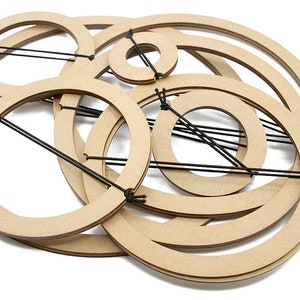 Puede incluir: Un conjunto de ocho aros de madera de diferentes tamaños, conectados por un cordel negro. Los aros están dispuestos en un patrón circular, creando un diseño decorativo y abstracto.
