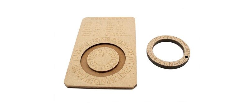 May include: A wooden Code Caesar cipher tool with a rotating wheel and a separate ring. The main piece has a chart and two rotating circles with letters and numbers. The ring has letters around its circumference. The text "CODE CEASAR" is visible.