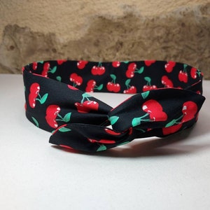 May include: A black headband with a cherry print. The headband is tied in a knot.