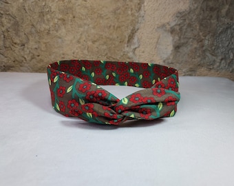 May include: A brown headband with a floral pattern featuring red flowers and green leaves.