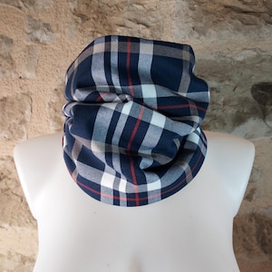 Peut inclure: Un tour de cou bleu marine à motif à carreaux. Le motif à carreaux comprend des rayures rouges, blanches et beiges. Le tour de cou est présenté sur un mannequin blanc. L'arrière-plan est un mur de pierre texturé brun clair.