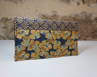 May include: A long, rectangular clutch purse with a floral pattern in shades of gold and blue on a dark blue background. The top half of the purse is a geometric pattern in gold and blue.