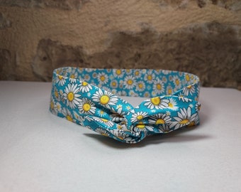 May include: A turquoise headband with a white daisy print. The headband is tied in a knot at the front.