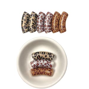 May include: A set of six leopard print hair scrunchies in various shades of brown, tan, and white. The scrunchies are arranged in a row and in a small white bowl.