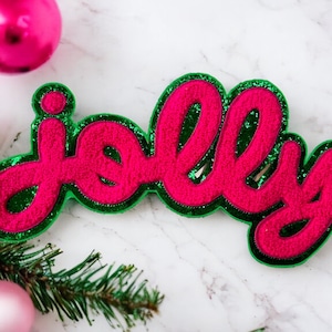 May include: A pink and green felt word sign that says "jolly".