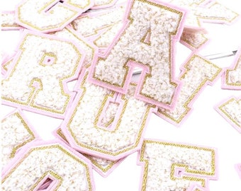 May include: A collection of pink felt letters with gold trim. The letters are all uppercase and are arranged in a random order. The letters are all approximately 7.5 cm tall.