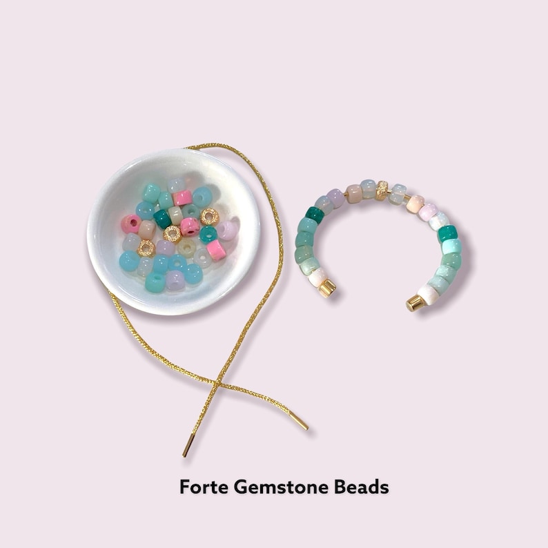 May include: An image featuring Forte Gemstone Beads in shades of pink, blue, green, and gold. A partially constructed bracelet is visible, alongside a gold string and a small white bowl. The text "Forte Gemstone Beads" is displayed at the bottom.
