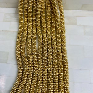 May include: A strand of gold-colored beads, each bead is small and round. The beads are strung together to form a long, continuous strand.