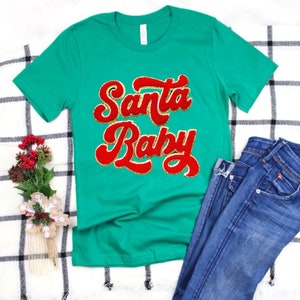 May include: A green t-shirt with the text "Santa Baby" in red and gold glitter lettering.