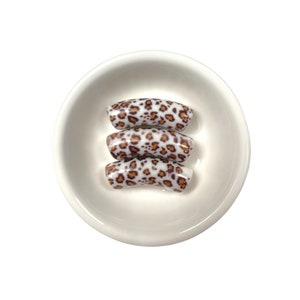 May include: Three white and brown leopard print nail tips in a small white bowl.