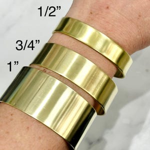 May include: Gold-colored metal cuff bracelets in three sizes: 1/2 inch, 3/4 inch, and 1 inch. The bracelets are stacked on a wrist, showcasing their width. The text "Casually Creative" is at the bottom.