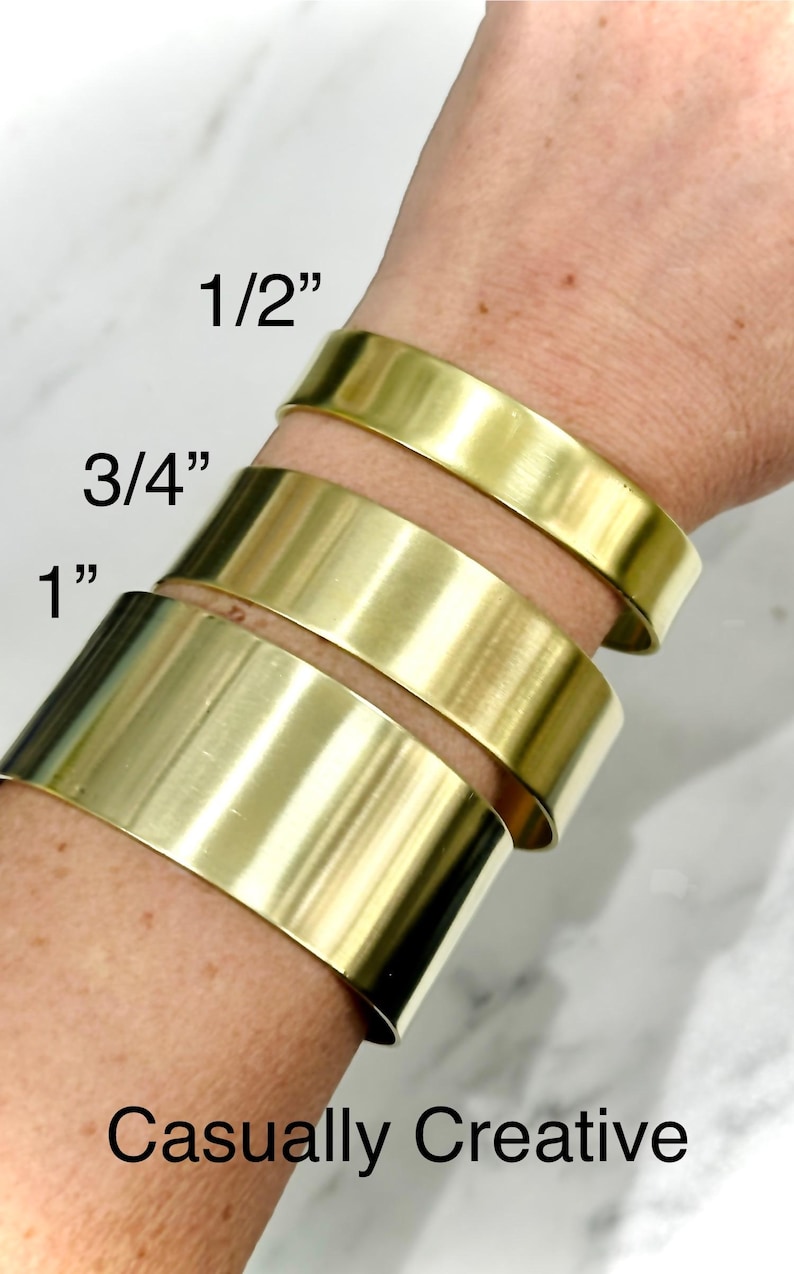 May include: Gold-colored metal cuff bracelets in three sizes: 1/2 inch, 3/4 inch, and 1 inch. The bracelets are stacked on a wrist, showcasing their width. The text "Casually Creative" is at the bottom.