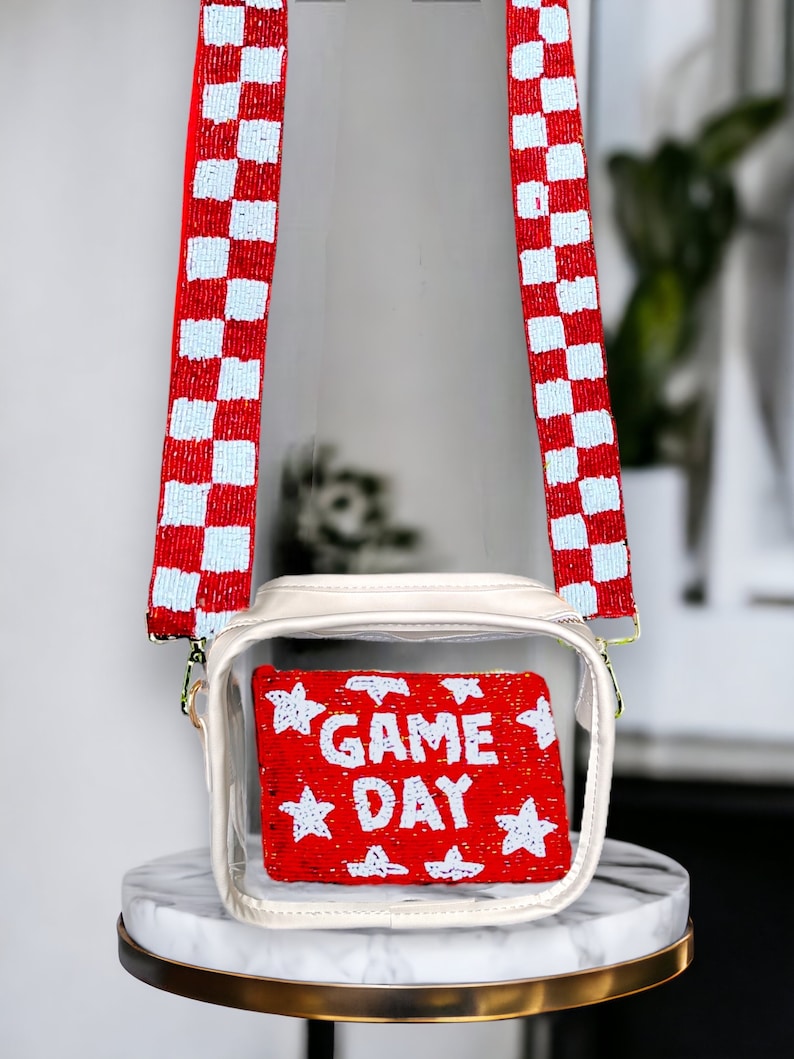 May include: Clear plastic crossbody bag with a red and white checkered beaded strap. The bag has a clear front panel that shows a red beaded clutch with white stars and the text "GAME DAY".