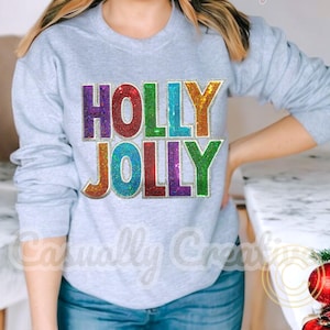May include: A light gray sweatshirt with the words "HOLLY JOLLY" in colorful, sequined letters. The text is in a rainbow of colors, including purple, red, blue, green, and gold. The sweatshirt is a crew neck style.