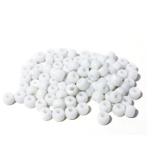 May include: A collection of white, cylindrical beads, each with a central hole. The beads are scattered, some appearing more rounded than others. These beads are suitable for jewellery making or various craft projects. The beads are opaque.