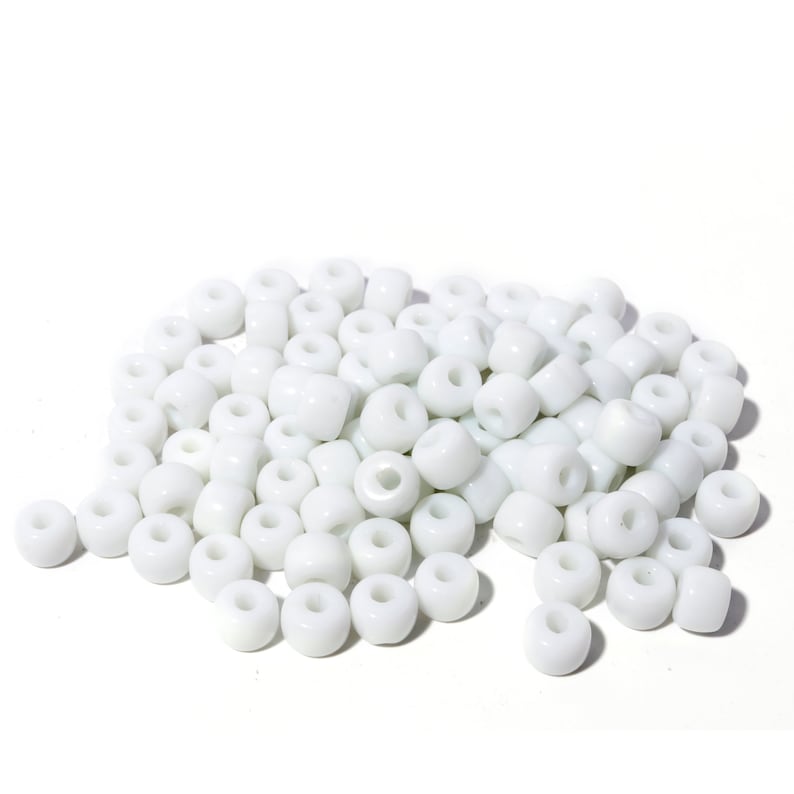 May include: A collection of white, cylindrical beads, each with a central hole. The beads are scattered, some appearing more rounded than others. These beads are suitable for jewellery making or various craft projects. The beads are opaque.