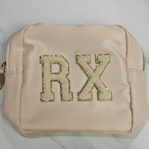May include: A light pink satin makeup bag with a gold zipper and the letters "RX" in gold glitter on the front.