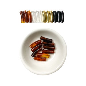 May include: A bowl filled with amber-colored hair barrettes. The barrettes are curved and have a glossy finish.