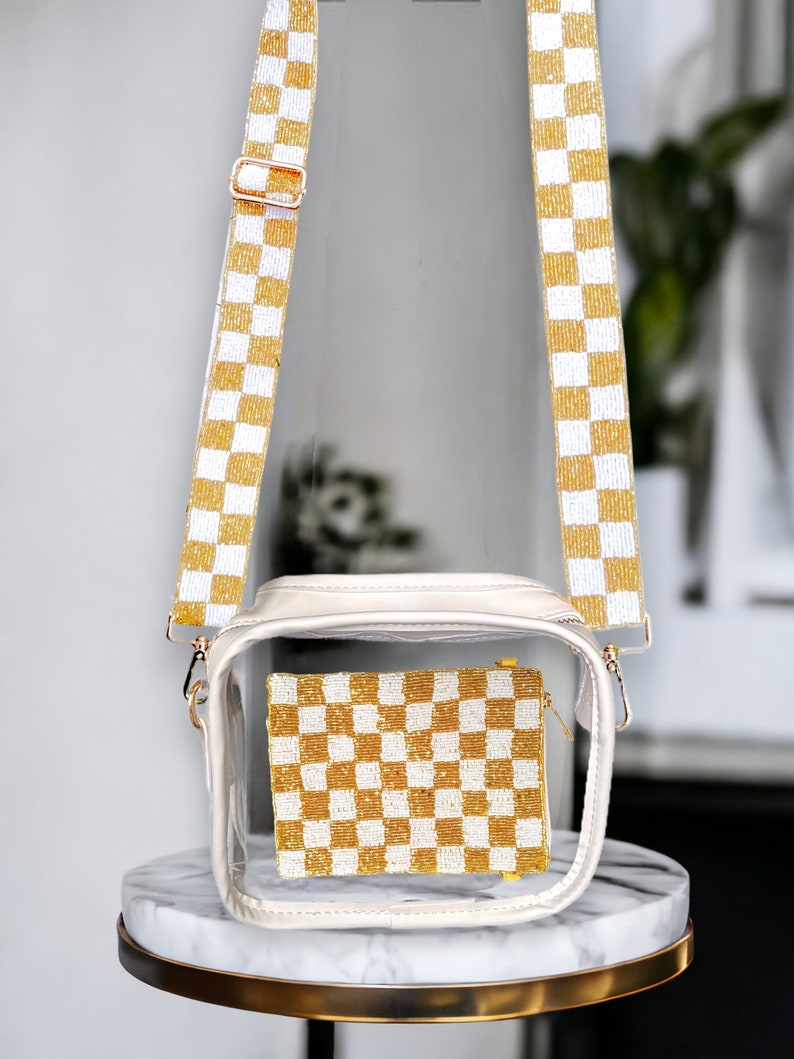 May include: A clear plastic crossbody bag with a white and gold checkered pattern. The bag has a zipper closure and a gold chain strap.