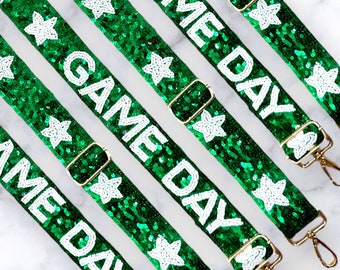 Może przedstawiać: Cztery zielone i białe paski z cekinami i złotymi klamrami. Każdy pasek ma napis "GAME DAY" w kolorze białym.