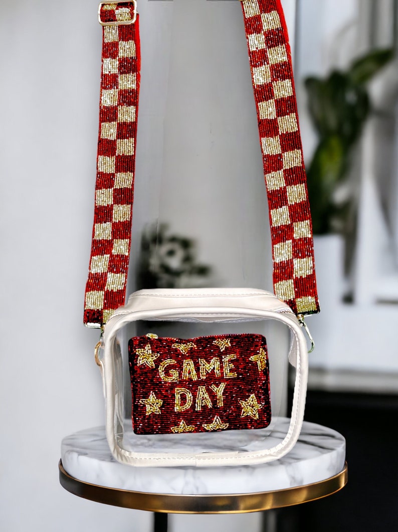 May include: Clear plastic crossbody bag with a red and gold checkered beaded strap. The bag has a white zippered pouch inside with a red beaded pouch that says "GAME DAY" in gold beads.