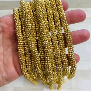 May include: A strand of gold-colored beads, each bead is a small sphere, the beads are strung together to form a long chain.