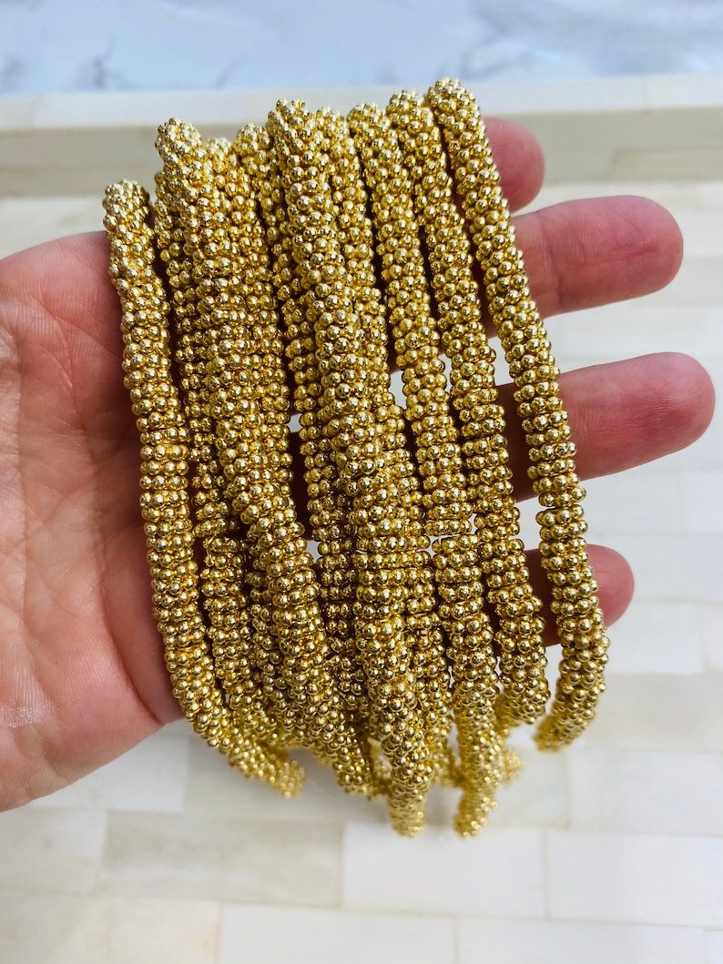May include: A strand of gold-colored beads, each bead is a small sphere, the beads are strung together to form a long chain.