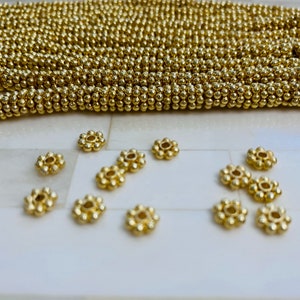May include: A close-up of gold-colored metal beads, some are round and some are shaped like small flowers.