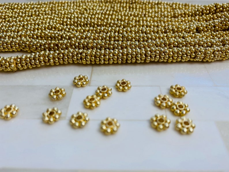 May include: A close-up of gold-colored metal beads, some are round and some are shaped like small flowers.