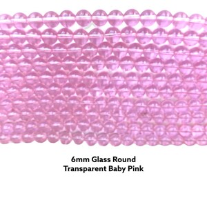 May include: A close-up of a strand of 6mm round glass beads in a transparent baby pink color.
