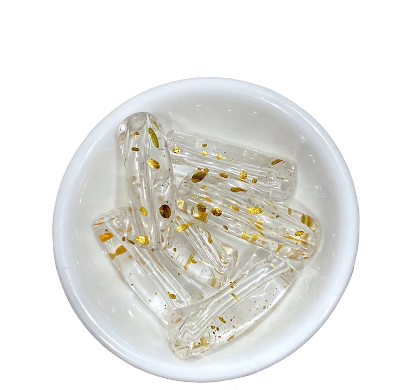 May include: A bowl of clear glass beads with gold flecks. The beads are cylindrical and have a slightly irregular shape.