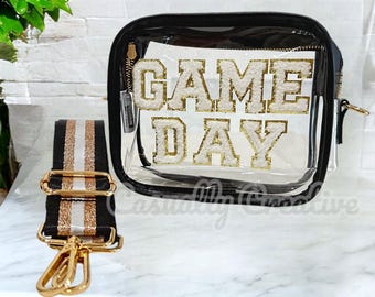 Puede incluir: Bolso transparente de plástico con cierre de cremallera dorado y ribete negro. El bolso tiene un diseño "GAME DAY" blanco y dorado en la parte delantera. El bolso viene con una correa ajustable de rayas negras y doradas.