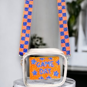 May include: Clear plastic crossbody bag with a white frame and a beaded orange and blue "GAME DAY" pouch inside. The bag has orange and blue checkered straps.