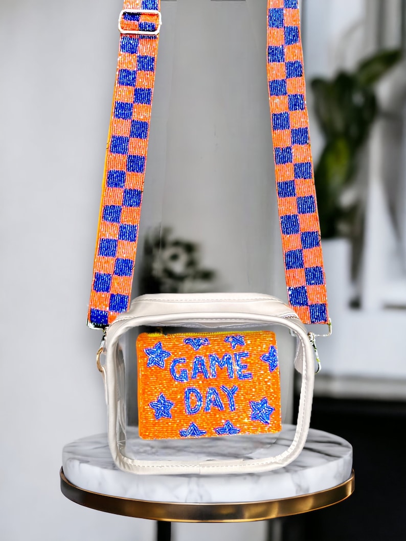 May include: Clear plastic crossbody bag with a white frame and a beaded orange and blue "GAME DAY" pouch inside. The bag has orange and blue checkered straps.