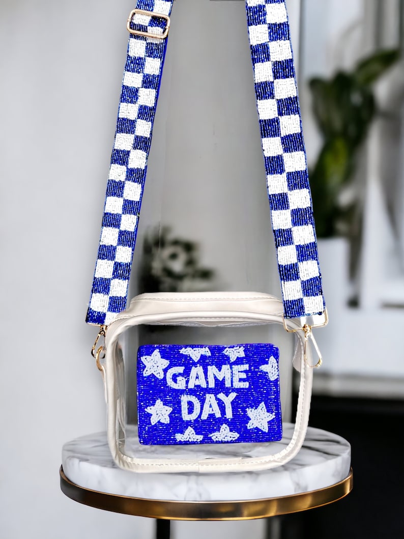 May include: A clear plastic crossbody bag with a white and blue checkered beaded strap. The bag has a white beaded patch with the words "GAME DAY" on it.