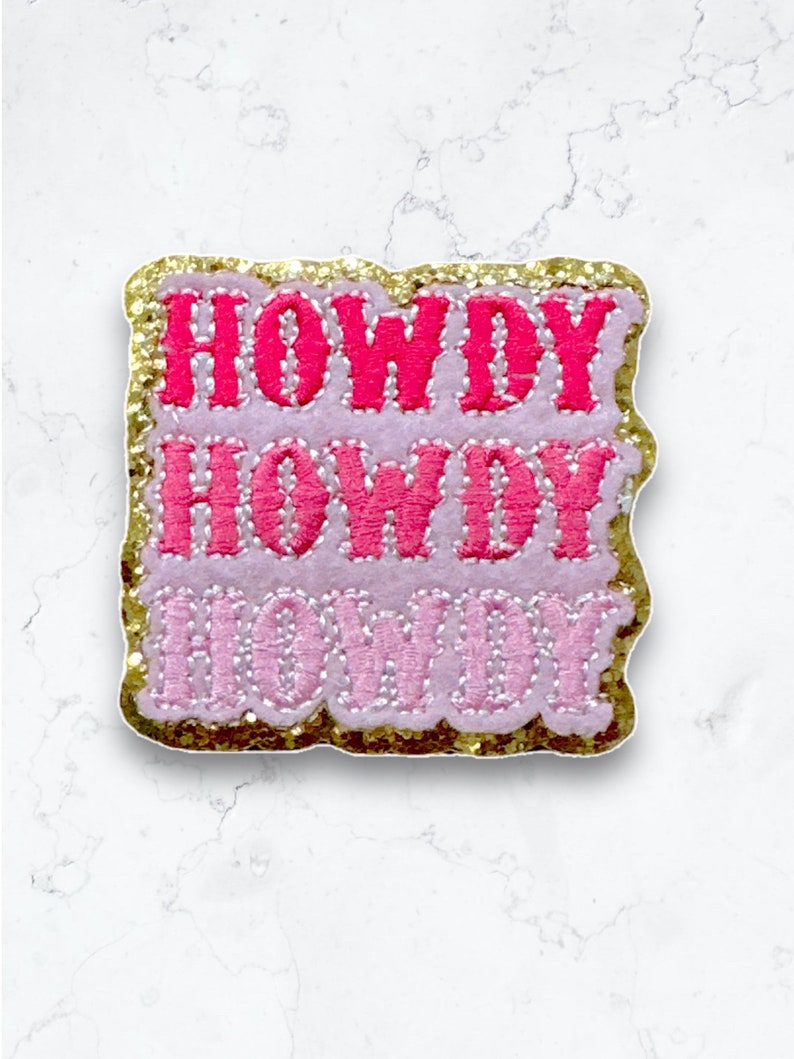 May include: A pink and gold glitter iron-on patch with the text "Howdy Howdy Howdy" in a retro font.