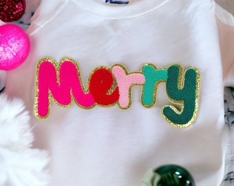 May include: White t-shirt with a colorful "Merry" embroidered patch. The letters are pink, red, light pink, green, and dark green with gold outlining.