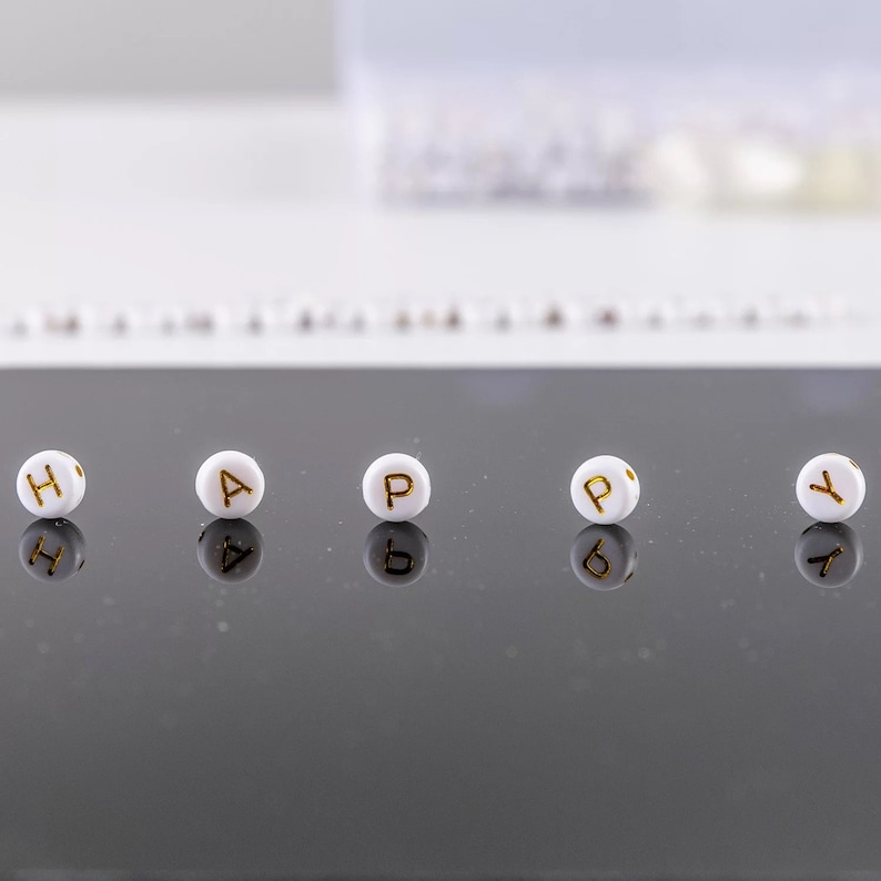May include: White letter beads spelling out the word "HAPPY" on a black reflective surface.