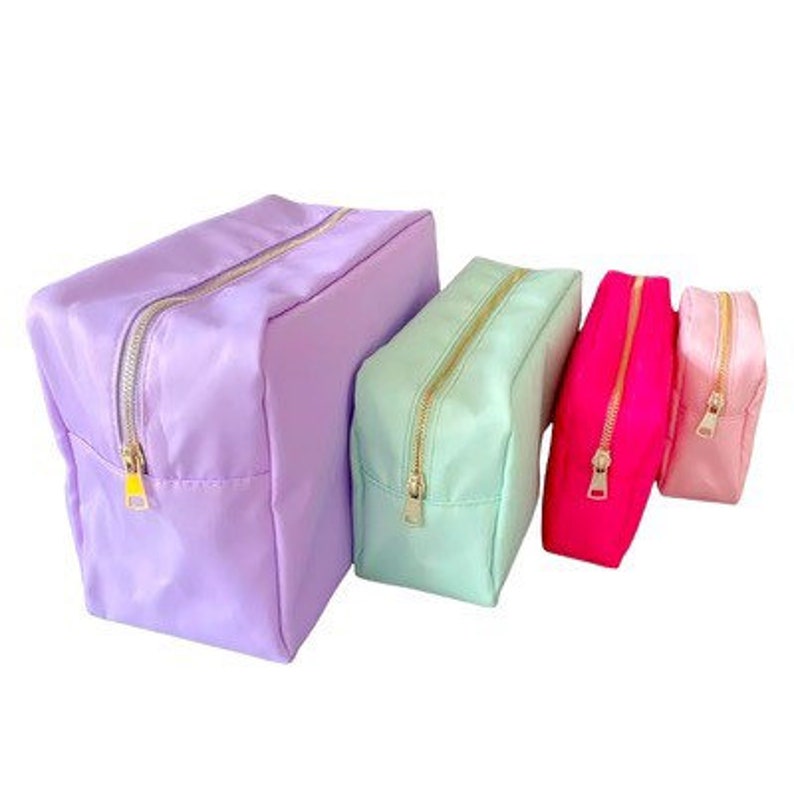 May include: Four zippered pouches in different sizes and colors. The largest pouch is lavender, the next is light green, the next is pink, and the smallest is light pink.