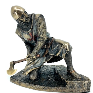 May include: A bronze statue of a kneeling crusader knight holding an axe. The knight is wearing chainmail armor and a red cross on his chest. The statue is on a base that looks like a rock.