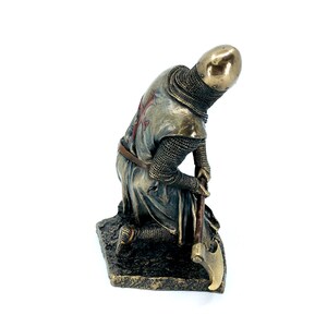 May include: A bronze statue of a kneeling crusader knight wearing chainmail armor and a red cross on his chest. He is holding a large axe in his right hand.