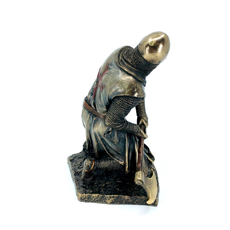 May include: A bronze statue of a kneeling crusader knight wearing chainmail armor and a red cross on his chest. He is holding a large axe in his right hand.