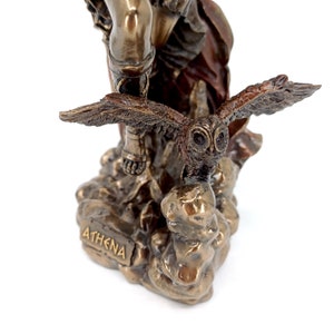 Puede incluir: Estatua de bronce de la diosa griega Atenea, de pie sobre una base rocosa con un b&uacute;ho posado en su mano. La estatua est&aacute; inscrita con la palabra "ATHENA" en la base.